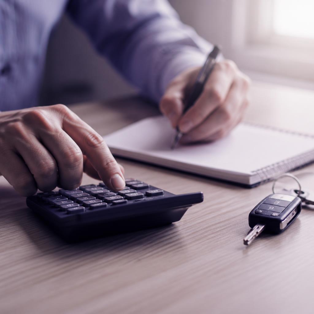 Hands using a calculator beside car keys