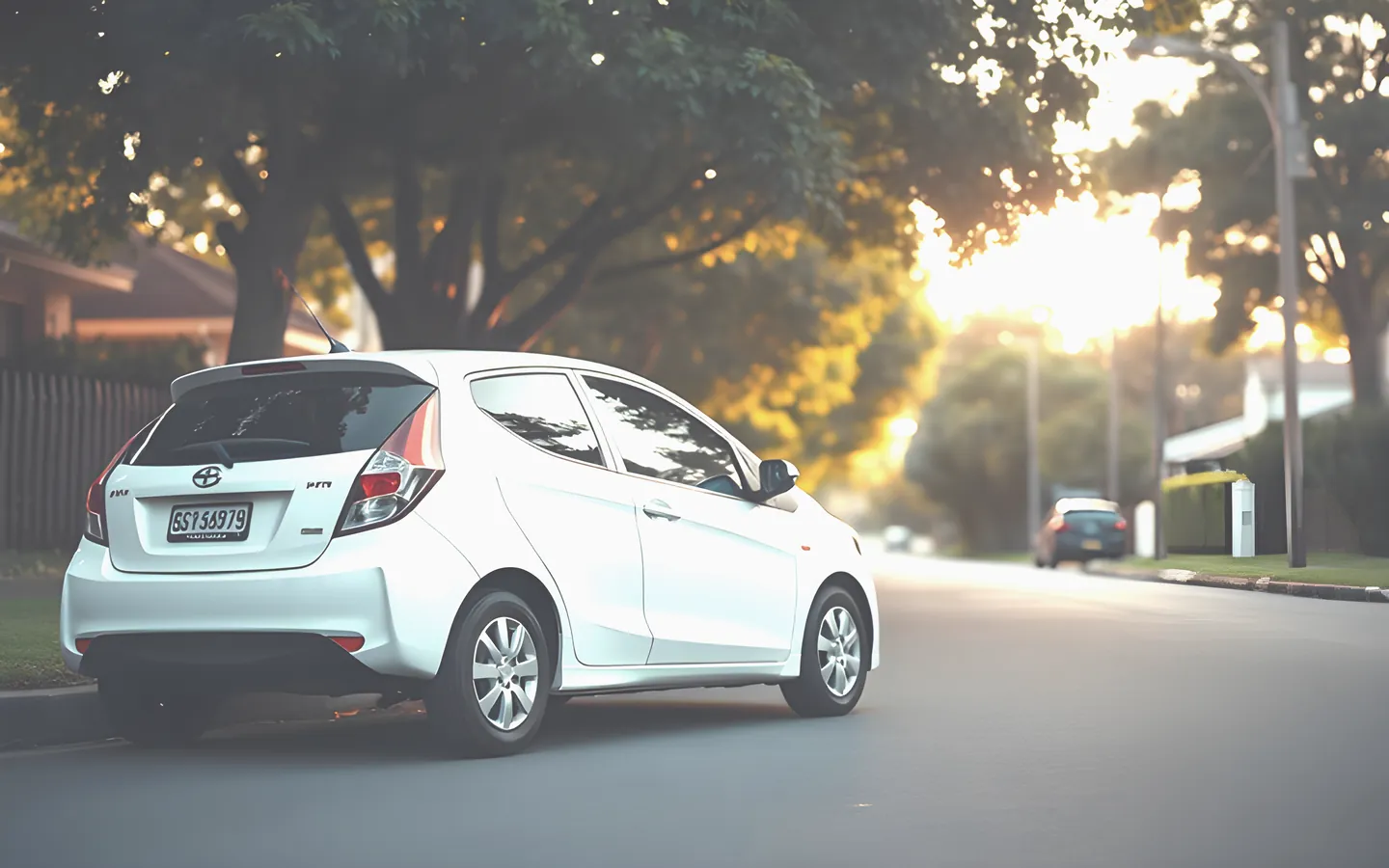 Small white hatchback parked on a leafy suburban street